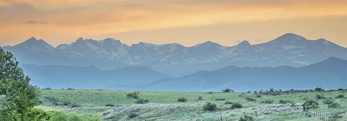 Mountain range with snow patches under a soft orange and yellow sunset sky